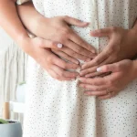 Image de quatre mains posées sur le ventre d'une femme pendant la période périnatale.